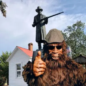 A man in a bigfoot costume and a statue of a person with a rifle.