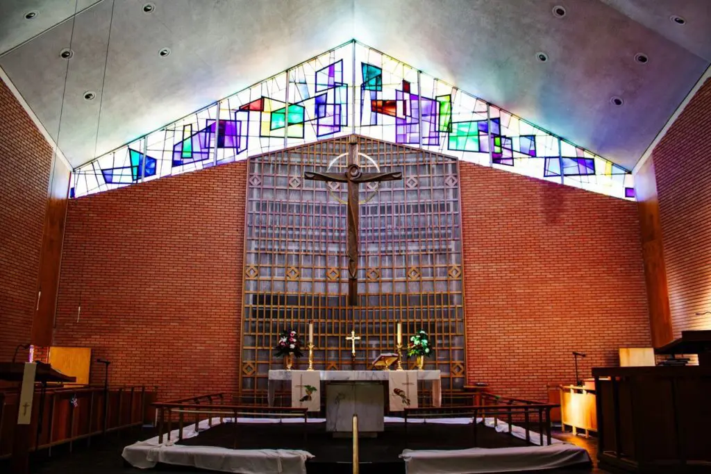Interior of a church featuring a crucifix, altar, and stained glass windows with colorful geometric patterns.