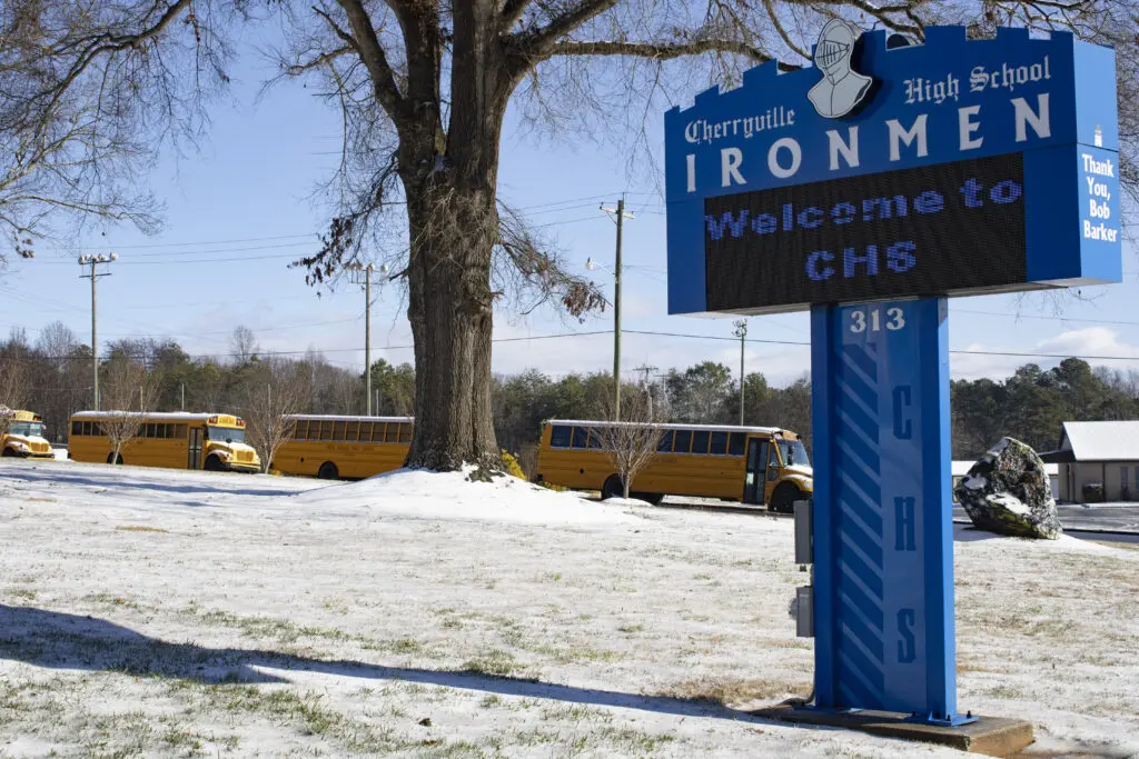 A wintery mix laying on the ground and buses and a large blue sign saying Cherryville High School Ironmen with a knights helmet on it.