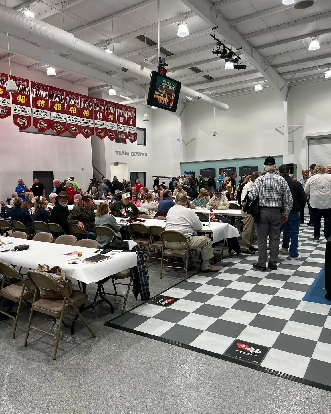 A group of people standing around tables with chairs.