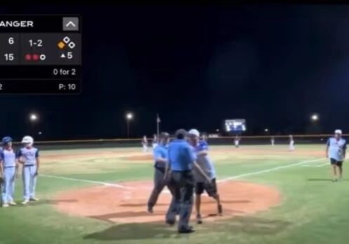 A nighttime baseball game with players and umpires gathered near home plate. The scoreboard shows Gamechanger 10-1, 6 BCLL 15, o-5. The count is 1-2 with two outs, top of the fifth inning.