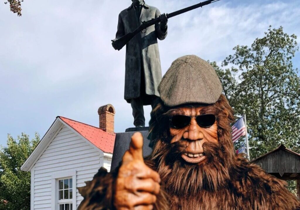 A man in a bigfoot costume and a statue of a person with a rifle.