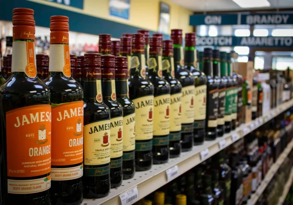 A row of various Jameson whiskey bottles on a store shelf, including Orange-flavored and traditional varieties.