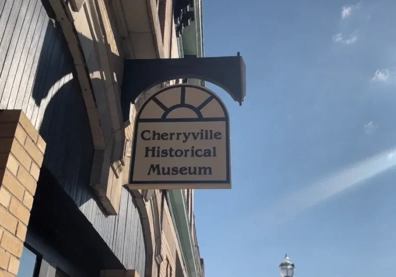 Sign for the Cherryville Historical Museum attached to the side of a building, with a clear blue sky in the background.